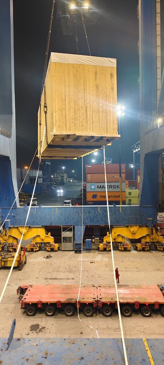 The oversized cargo unit on a multi-axle trailer, in transit through the port at dawn
